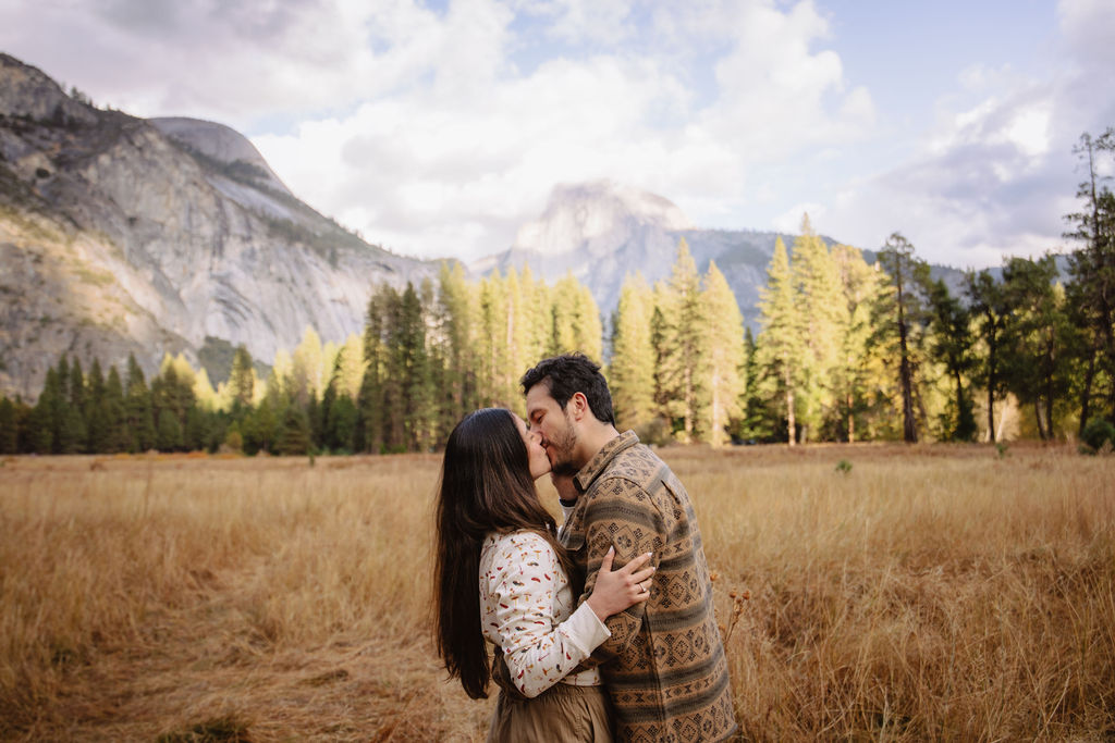 A couple stands in a sunlit field surrounded by trees, looking at each other affectionately. Sunlight creates a warm, golden glow taken by a yosemite proposal photographer