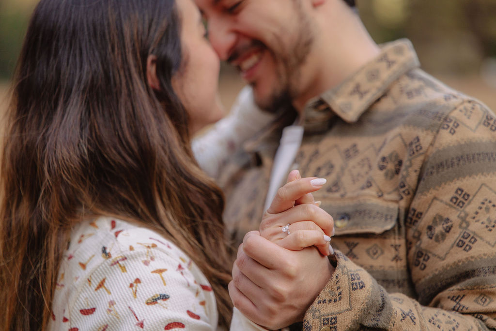 A couple stands in a sunlit field surrounded by trees, looking at each other affectionately. Sunlight creates a warm, golden glow taken by a yosemite proposal photographer