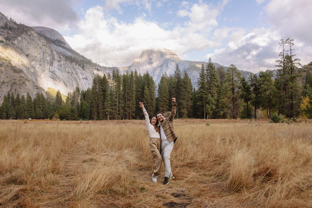 A couple stands in a sunlit field surrounded by trees, looking at each other affectionately. Sunlight creates a warm, golden glow taken by a yosemite proposal photographer