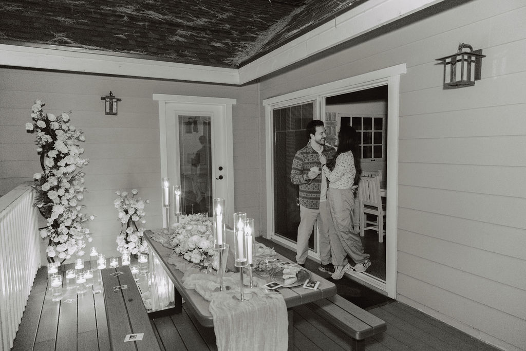 A couple embraces on a patio decorated with candles, flowers, and a table set for a meal.