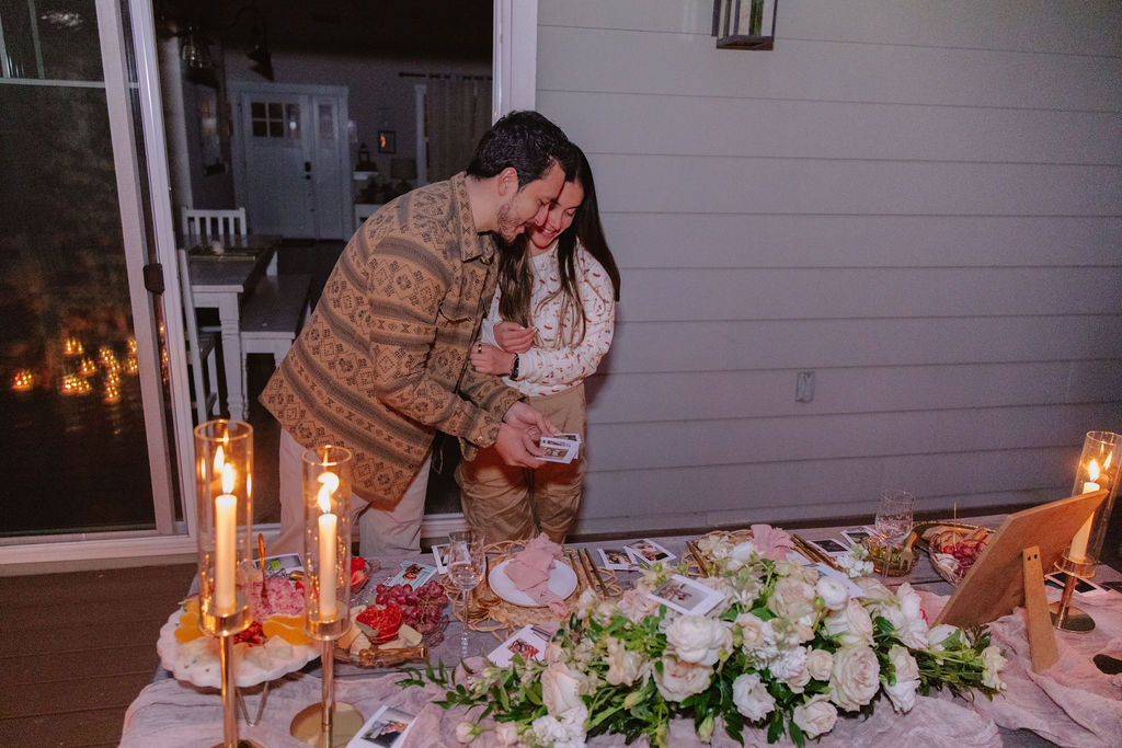 A couple embraces on a patio decorated with candles, flowers, and a table set for a meal.