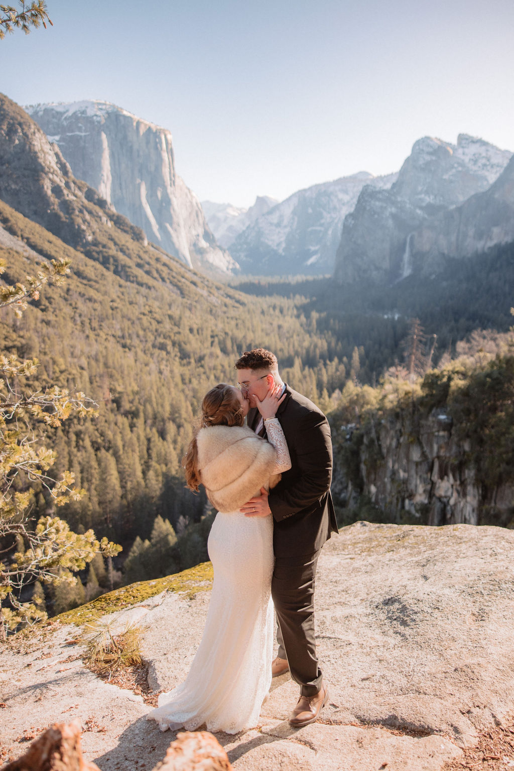 Bride in a white gown and veil stands on a rocky outcrop, with a mountain landscape in the background for an elopement in california