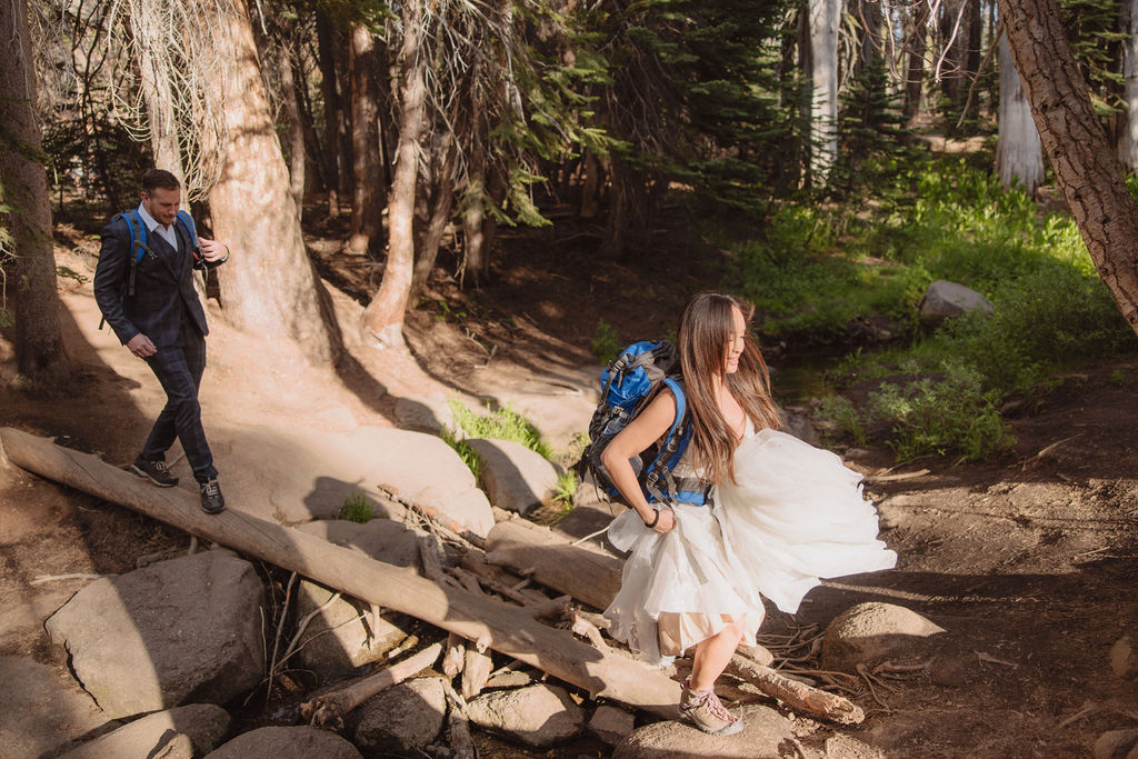 A couple embraces in a forested area, with tall trees surrounding them and sunlight filtering through the branches. | What to Wear for Your Yosemite Elopement