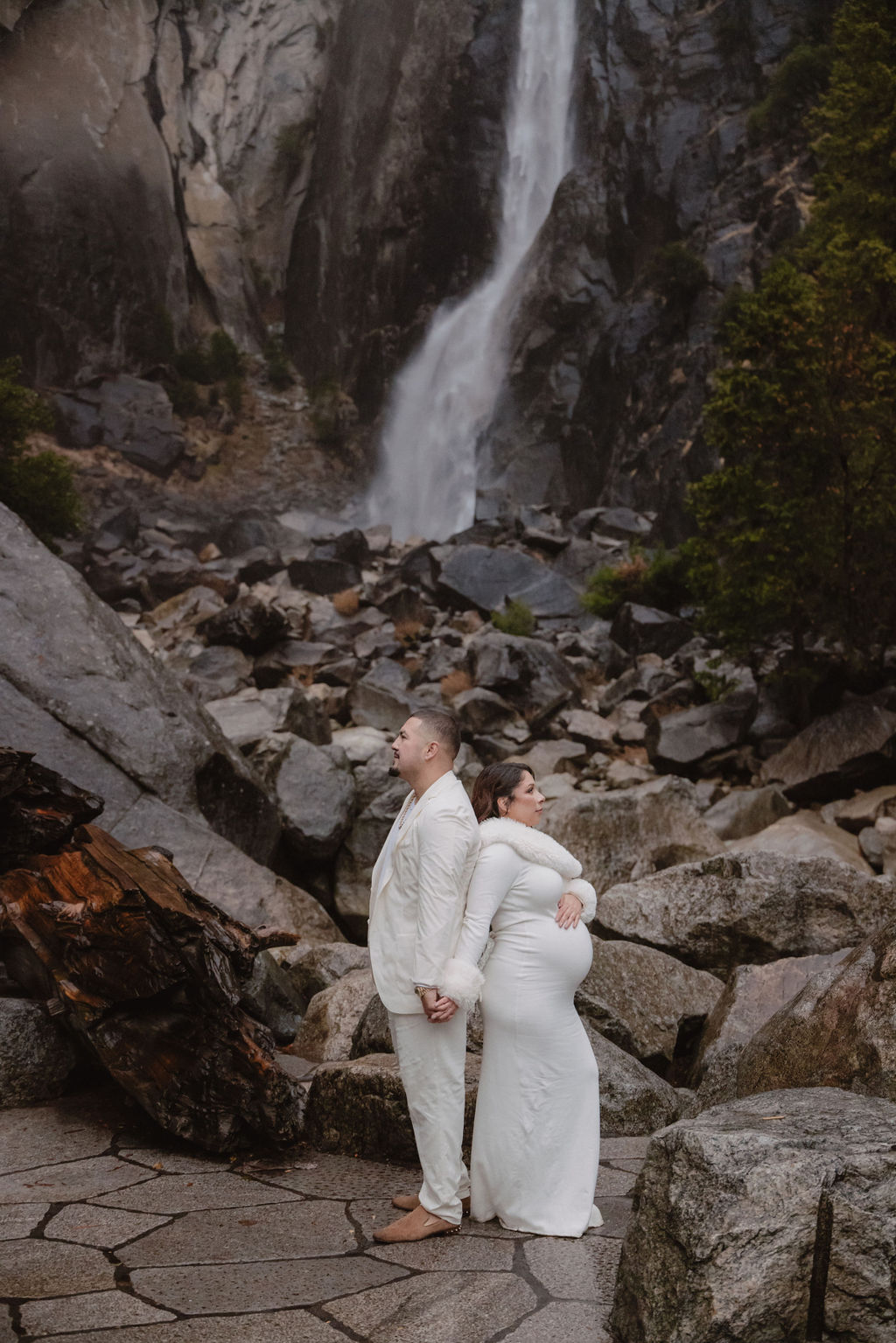 Woman in a white dress stands in front of a rocky landscape with a waterfall in the background.