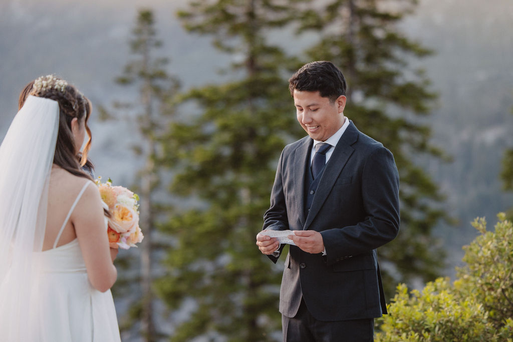 A couple stands on a rocky ledge, exchanging vows with an officiant. The background features a large mountain, likely Half Dome in Yosemite. How to Include Friends & Family in Your Elopement