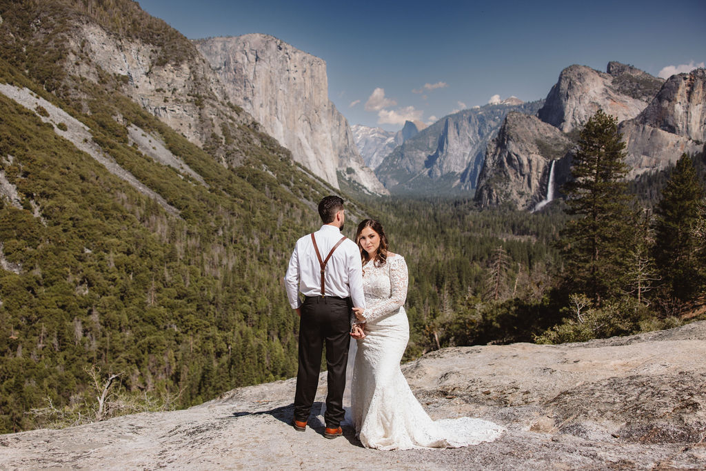 Bride and groom standing on a rocky ledge with a vast mountain landscape and valley in the background for an elopement in California