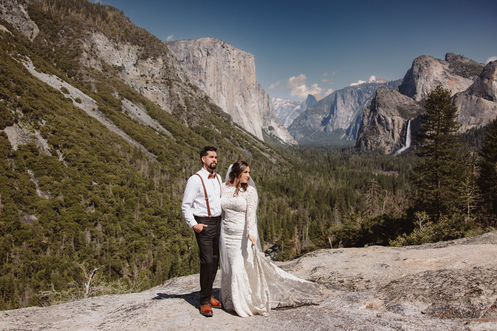 Bride and groom standing on a rocky ledge with a vast mountain landscape and valley in the background for an elopement in California