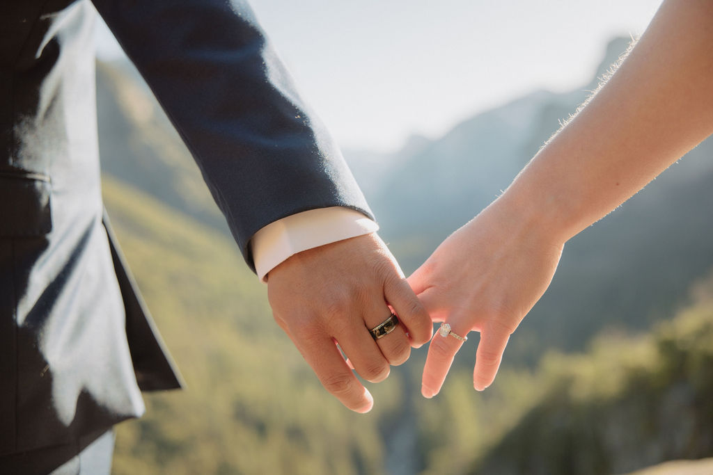 A bride and groom on a rocky ledge with mountains and forest in the background, under daylight for their sunrise yosemite elopement