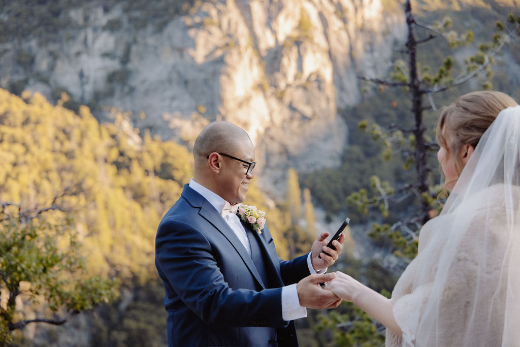 A bride and groom on a rocky ledge with mountains and forest in the background, under daylight for their sunrise yosemite elopement