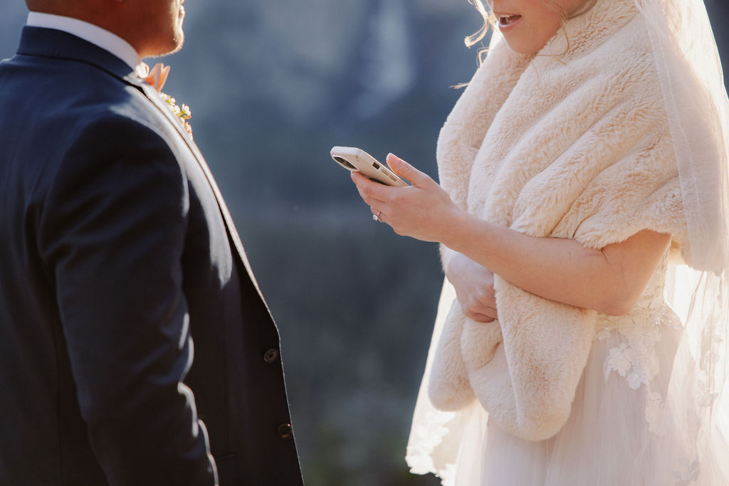 A bride and groom on a rocky ledge with mountains and forest in the background, under daylight for their sunrise yosemite elopement