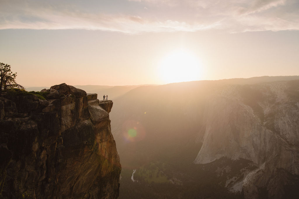 A bride and groom stand on rocky terrain, holding hands and facing a scenic mountain view at sunset. The Best Time for a Yosemite Elopement