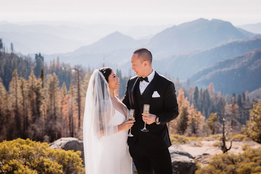 A small wedding ceremony takes place outdoors on a mountaintop, with guests standing and mountains visible in the background for their adventure elopement at sequoia national park