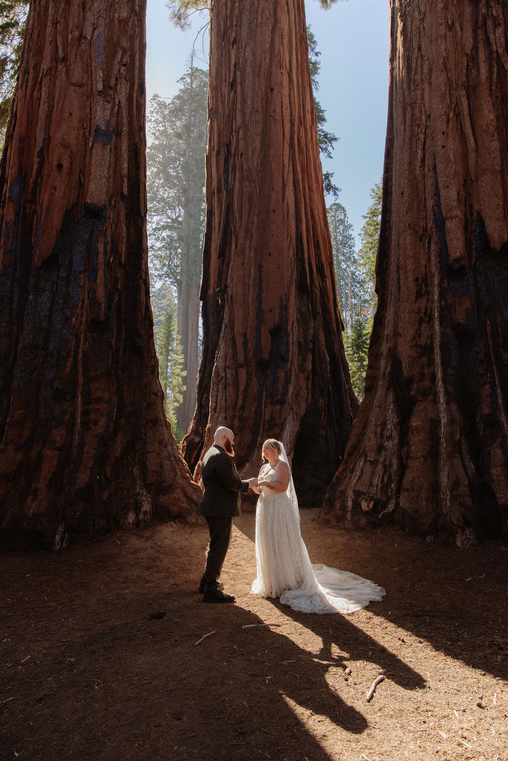 A bride and groom stand holding hands in front of giant redwood trees in a forest for their elopement in Yosemite and Sequoia