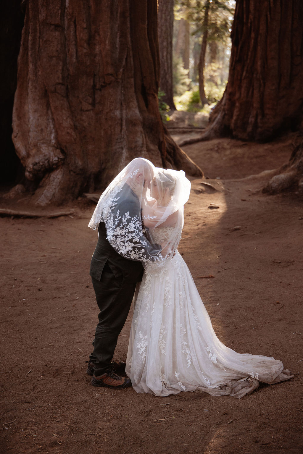 A bride and groom stand holding hands in front of giant redwood trees in a forest for their elopement in Yosemite and Sequoia