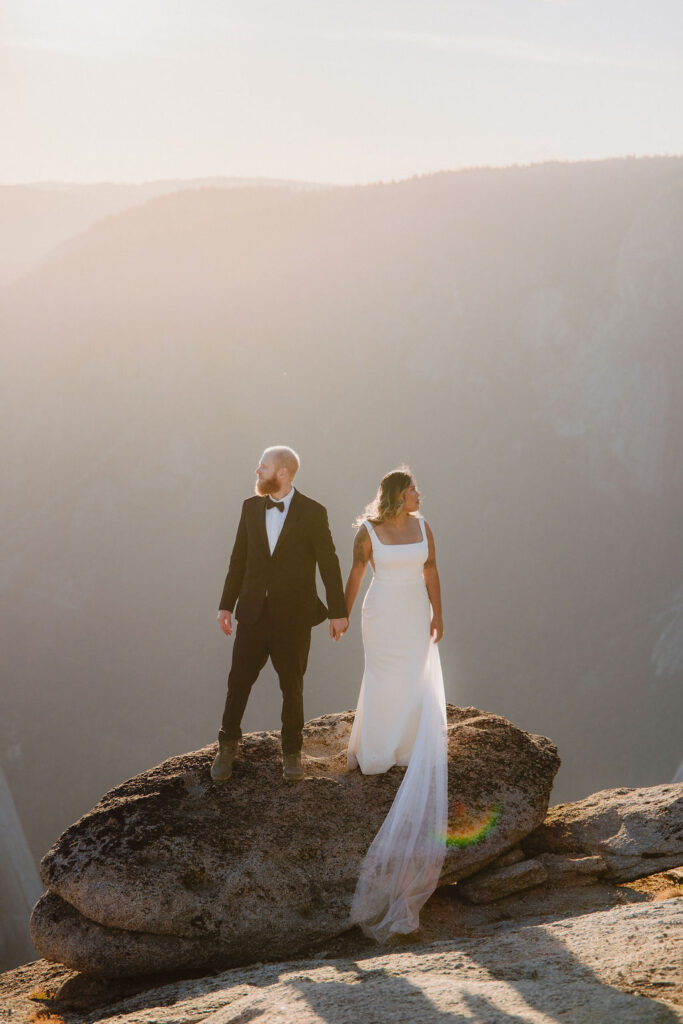 A person stands on the edge of a rocky cliff at sunset, overlooking a vast valley with distant mountains and a river below for their unique elopement