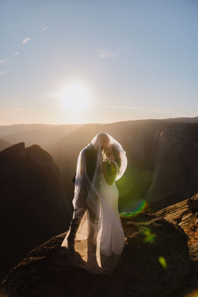 A person stands on the edge of a rocky cliff at sunset, overlooking a vast valley with distant mountains and a river below for their unique elopement