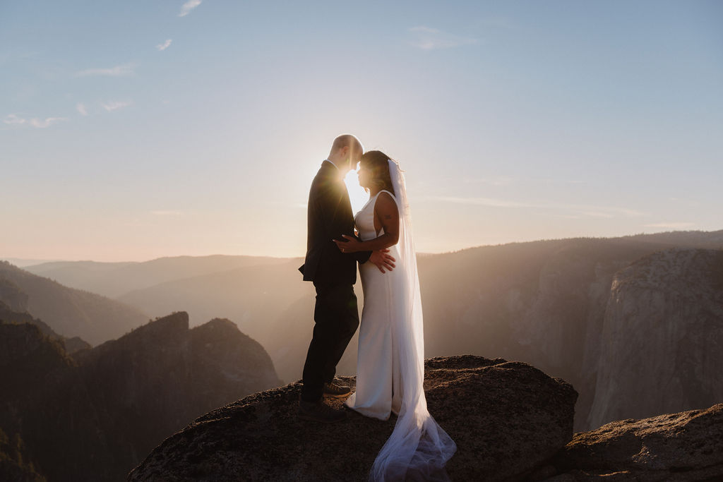 A person stands on the edge of a rocky cliff at sunset, overlooking a vast valley with distant mountains and a river below for their unique elopement