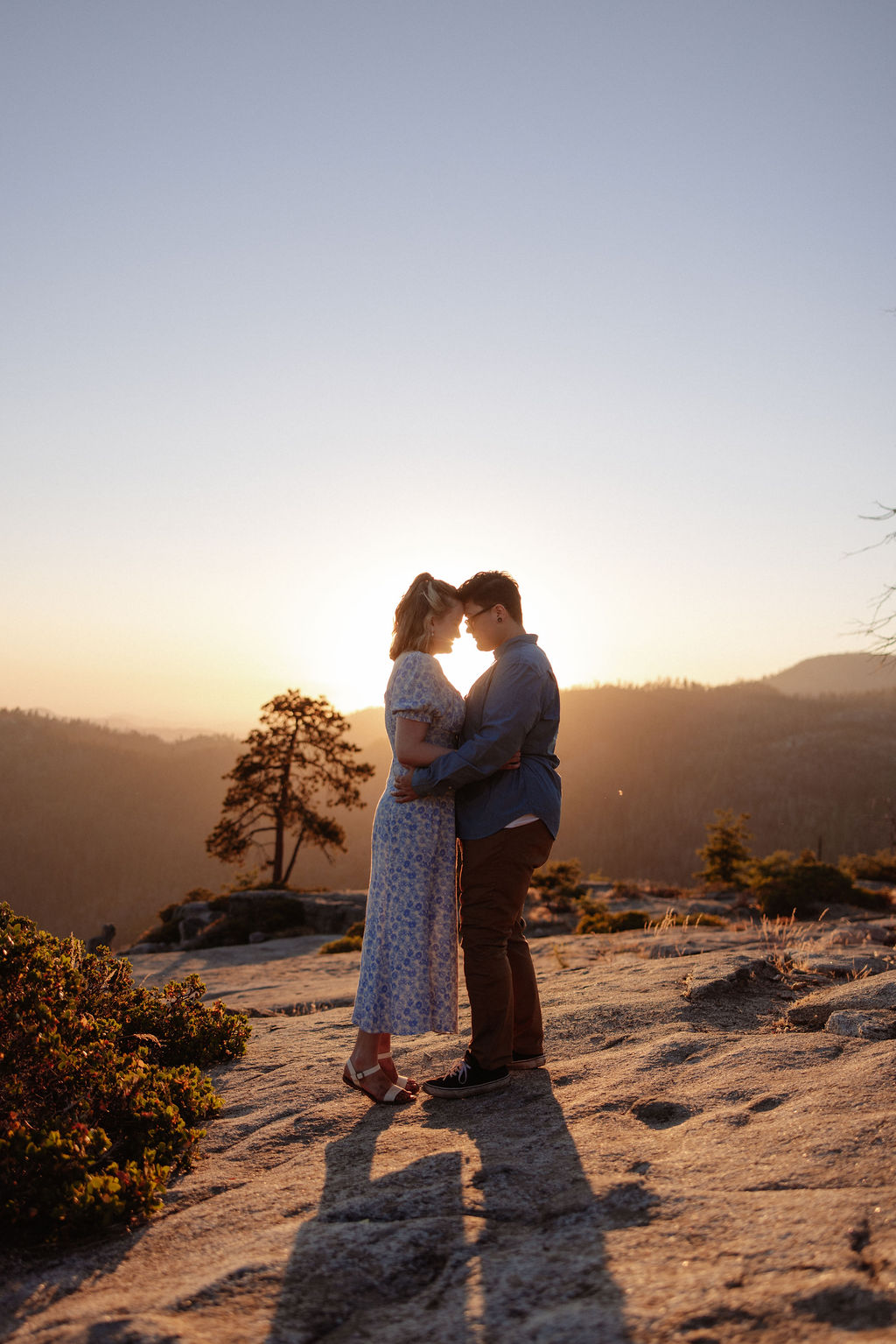 A couple holding hands walks on a rocky surface overlooking a scenic mountain landscape at sunset for their sequoia national park engagement photos