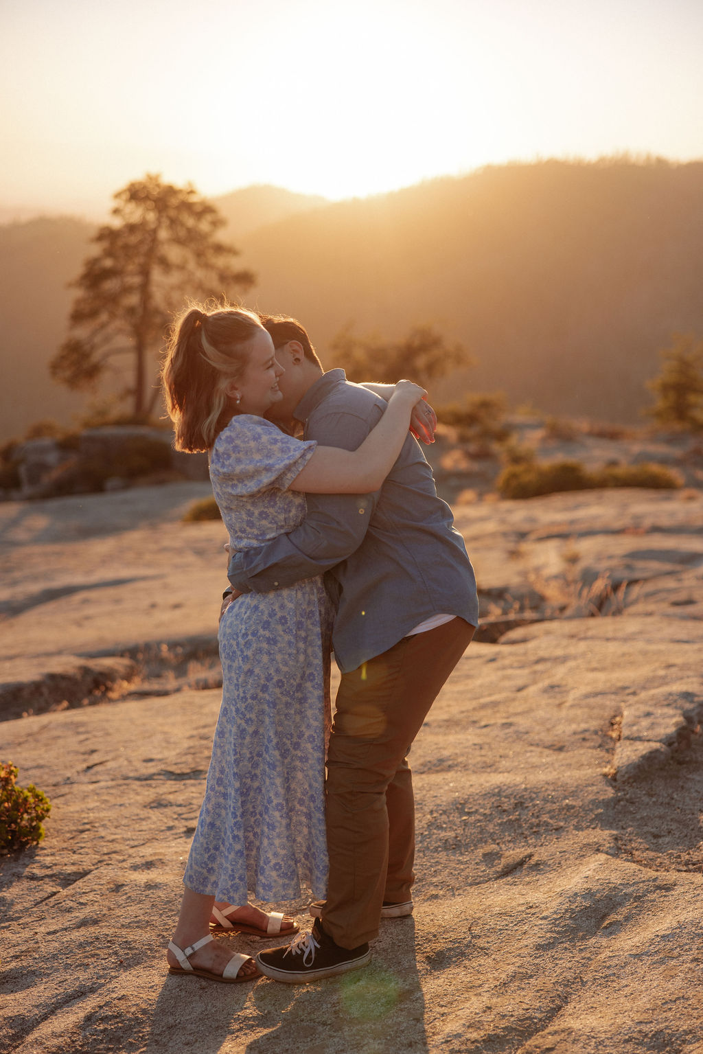 A couple holding hands walks on a rocky surface overlooking a scenic mountain landscape at sunset for their sequoia national park engagement photos
