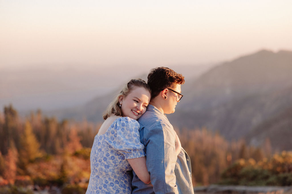 A couple holding hands walks on a rocky surface overlooking a scenic mountain landscape at sunset for their sequoia national park engagement photos