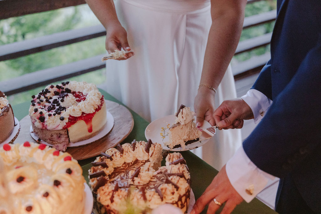 A bride and groom stand together on a decorated outdoor deck, surrounded by set dining tables with floral centerpieces and scenic mountain views in the background.