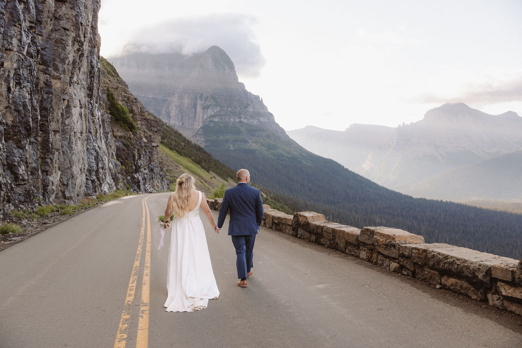 A couple dressed in formal attire stands closely together outdoors, with mountains and greenery in the background or a wedding at glacier national park