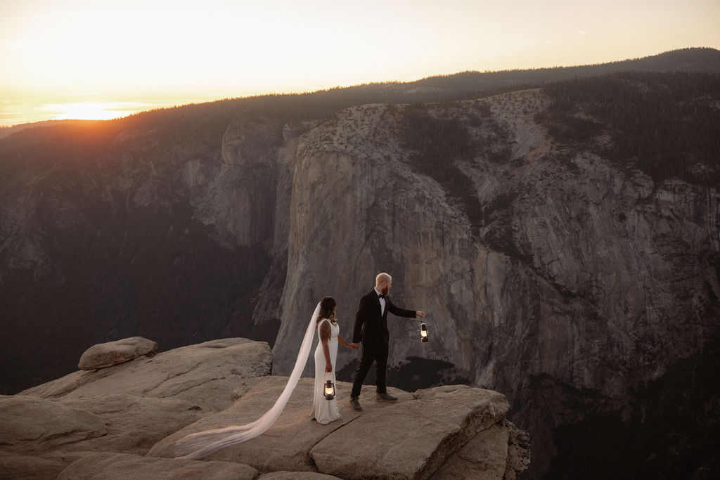 A bride and groom stand on a rocky cliff edge at sunset with mountains and a valley in the background for a glacier point elopement