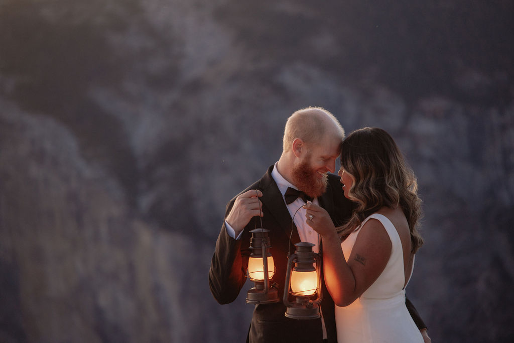 A bride and groom stand on a rocky cliff edge at sunset with mountains and a valley in the background for a glacier point elopement