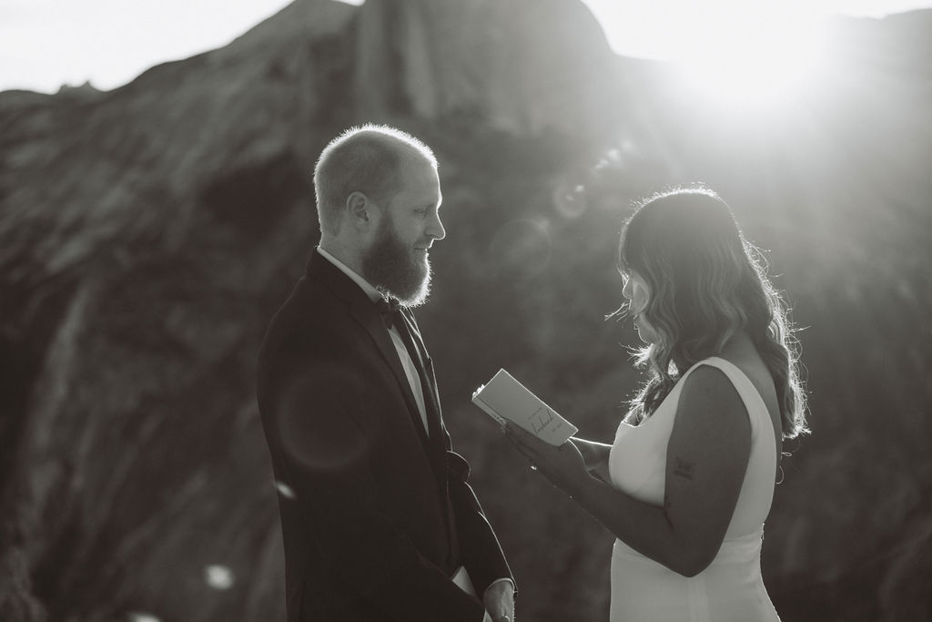 A couple stands on a rocky overlook exchanging vows at sunset, with mountains and Half Dome in the background for a glacier point elopement