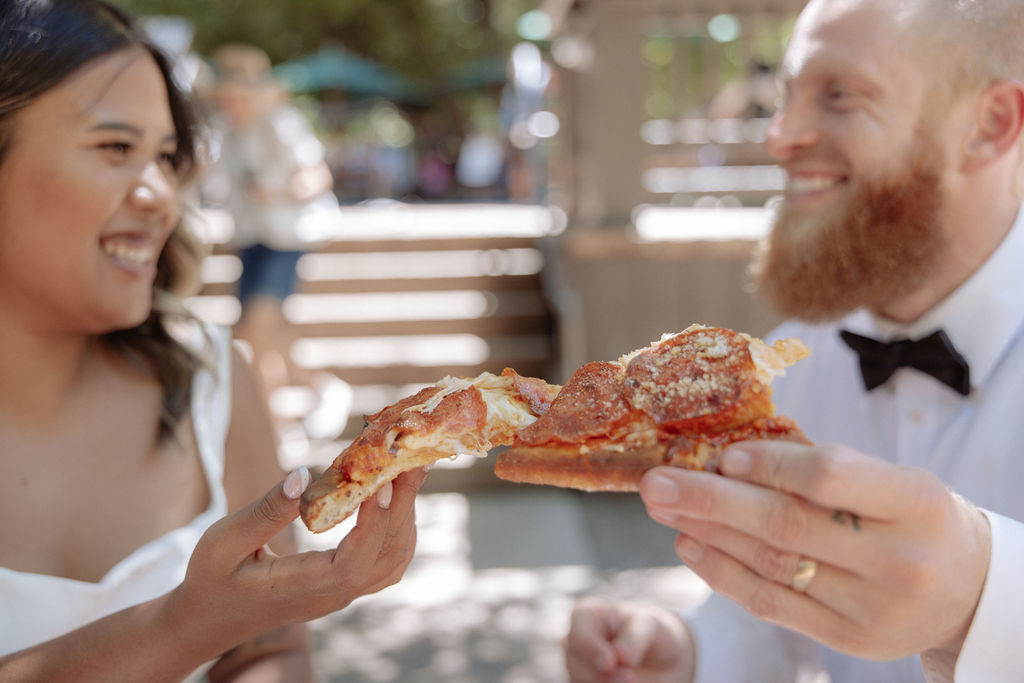 A woman and a man sit at an outdoor table sharing a pizza, each reaching for a slice. Two large drinks are on the table in front of them for a glacier point elopement 