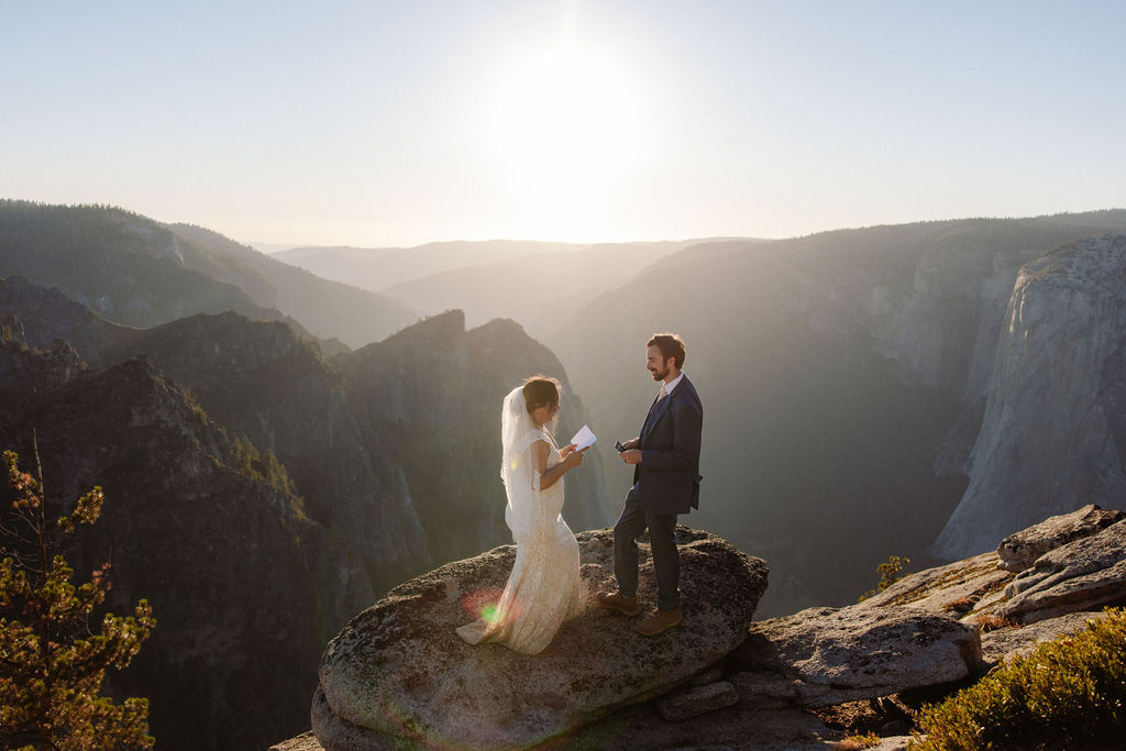 A bride and groom stand together on a rocky cliff at sunset with mountains in the background for a wedding at Yosemite
