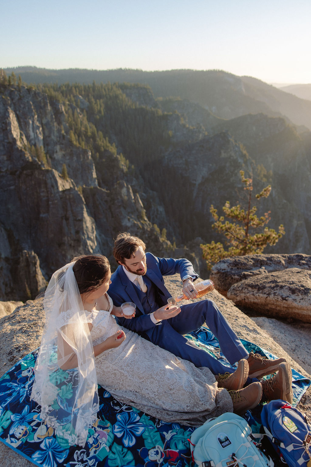 A bride and groom stand together on a rocky cliff at sunset with mountains in the background for a wedding at Yosemite