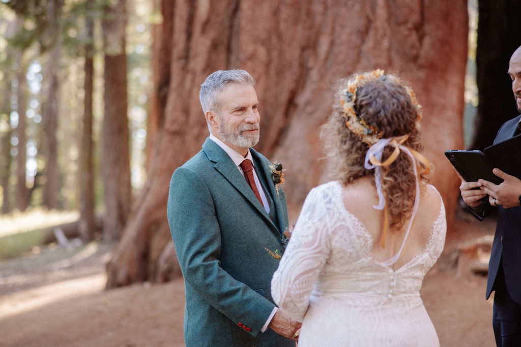 A couple stands with an officiant among giant redwood trees during a wedding ceremony in a forest setting taken. y a sequoia elopement photographer