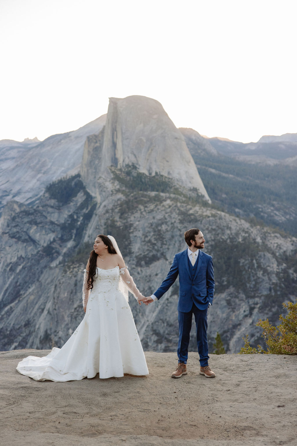 A bride and groom stand together on a rocky ledge with a large mountain peak in the background for a wedding at yosemite
