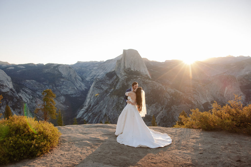 A bride and groom stand together on a rocky ledge with a large mountain peak in the background for a wedding at yosemite