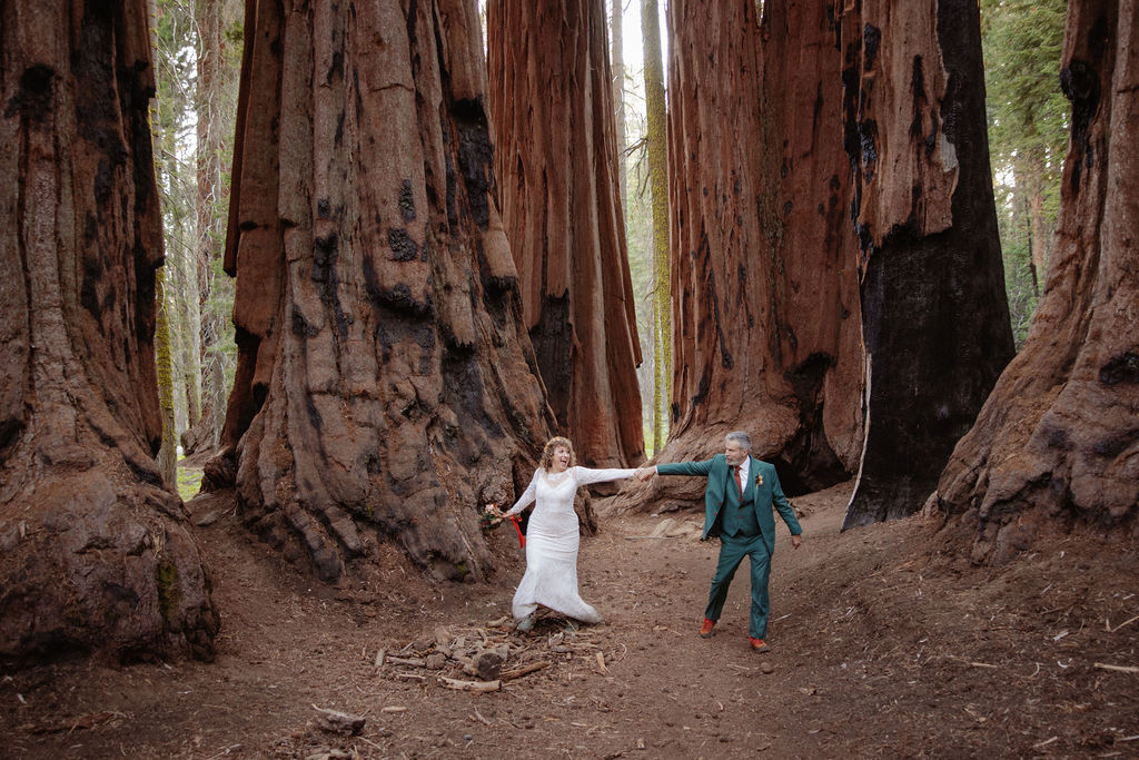 A couple stands embraced on a forest path between towering redwood trees taken by a sequoia elopement photographer