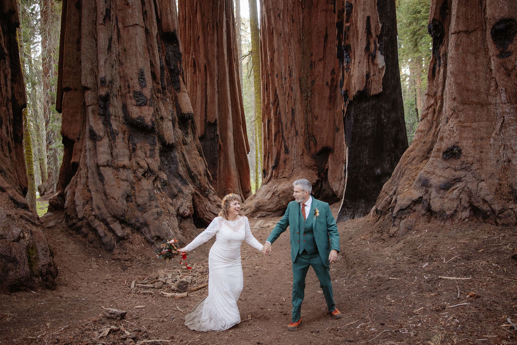A couple stands embraced on a forest path between towering redwood trees taken by a sequoia elopement photographer