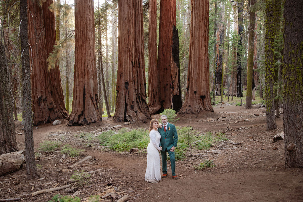 A couple stands embraced on a forest path between towering redwood trees taken by a sequoia elopement photographer