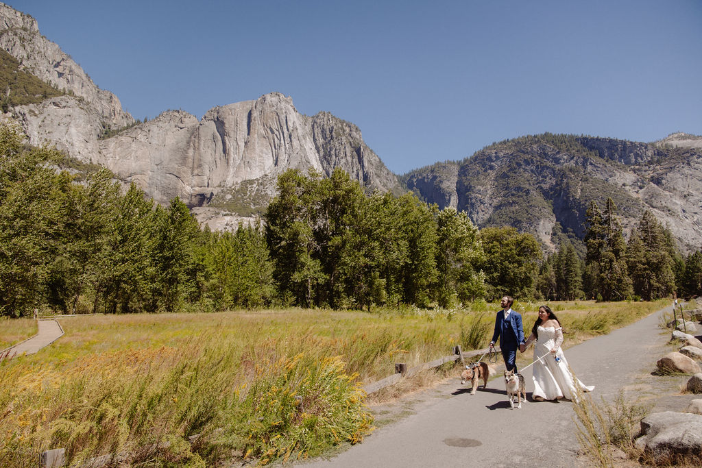 A bride and groom stand together, holding hands and touching foreheads, on a sandy area with mountains and trees in the background for a wedding at Yosemite