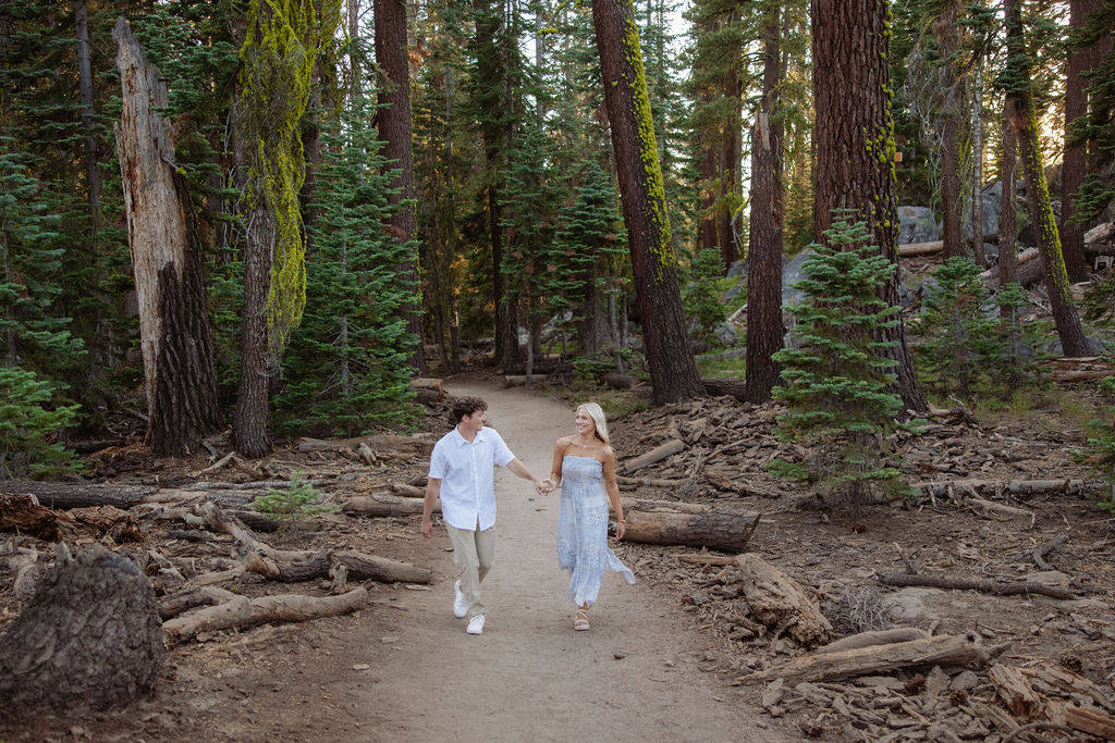 A couple stands together in a sunlit forest clearing, surrounded by tall trees and green foliage.