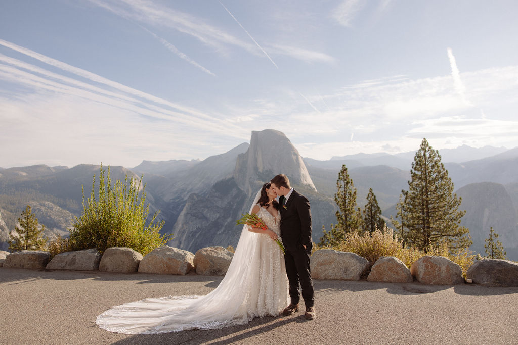 Bride and groom hold hands during an outdoor wedding ceremony with an officiant, set against a mountainous backdrop.