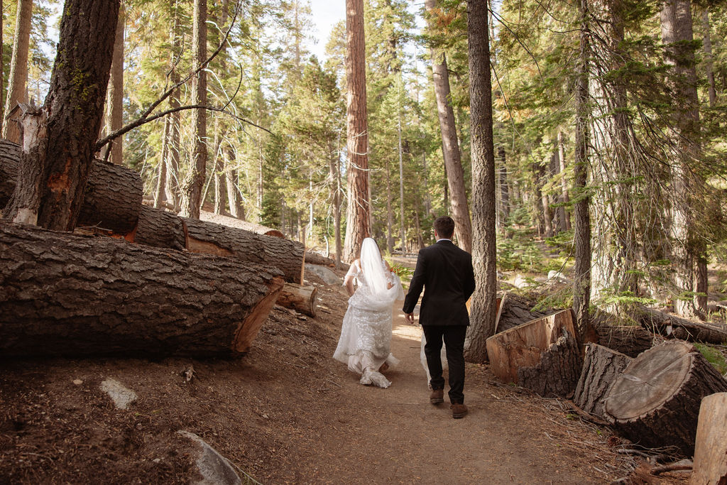 A bride and groom stand on rocky terrain overlooking a scenic mountain landscape at sunset, with the bride wearing a long white dress and veil for an elopement in Yosemite in September