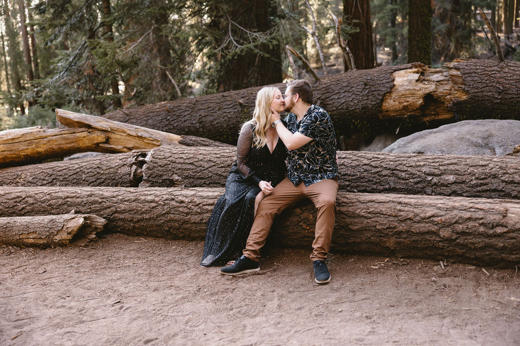 A man and a woman stand holding hands in front of a giant sequoia tree in a forest, both looking away from each other. Sequoia National Park Spots for Photos