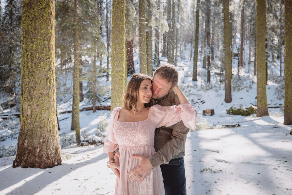 Two people stand in the hollow trunk of a large sequoia tree surrounded by tall trees and patches of snow at a Sequoia National Park Spots for Photos