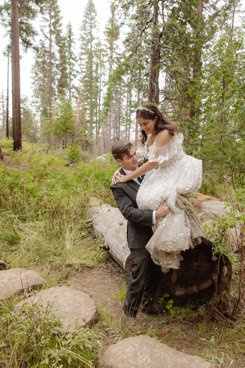 A bride and groom stand together in a forest, looking at each other, surrounded by tall trees and natural greenery for an elopement in Yosemite in September