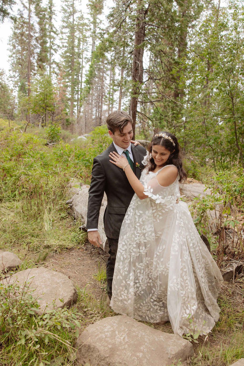 A bride and groom stand together in a forest, looking at each other, surrounded by tall trees and natural greenery for an elopement in Yosemite in September