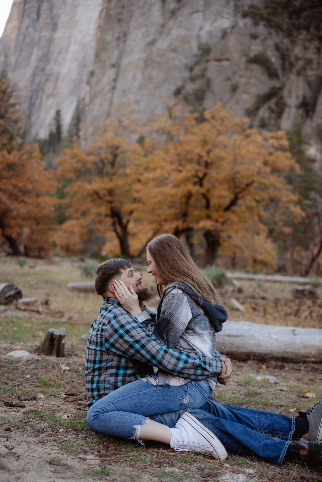 Woman sits in mans lap during casual Yosemite Valley engagement photoshoot