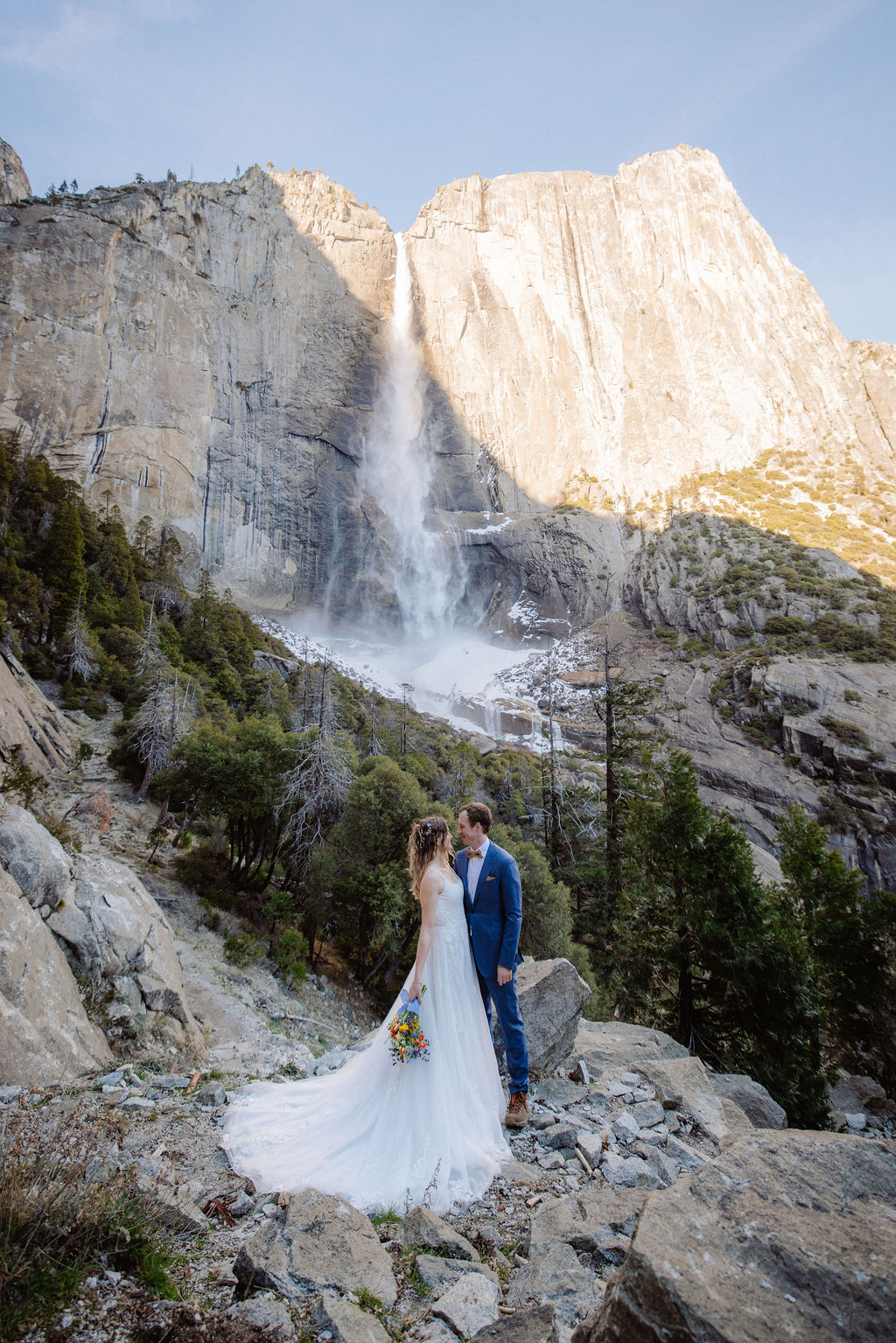 Bride and groom pose on hike in Yosemite with waterfall backdrop
