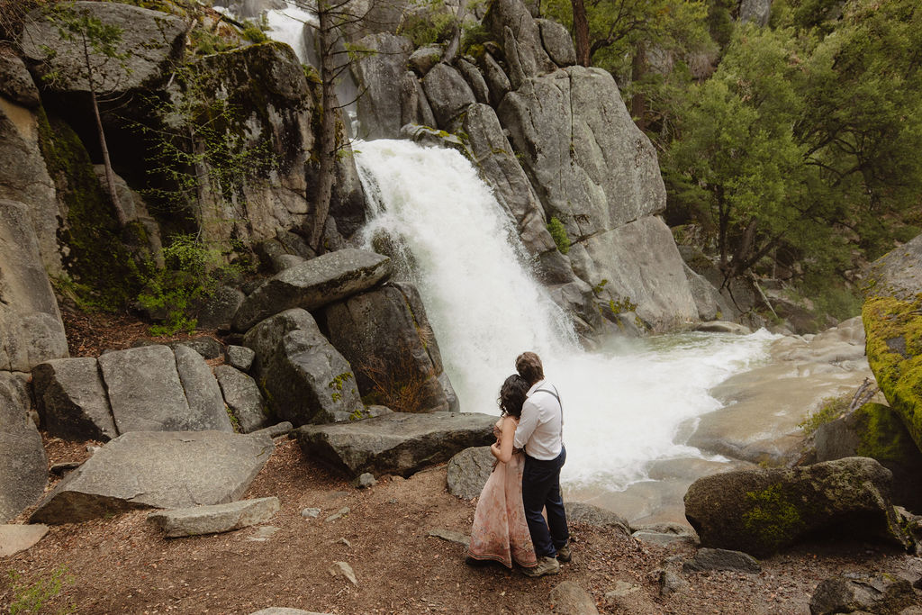 Couple admires waterfall during proposal photos in Yosemite
